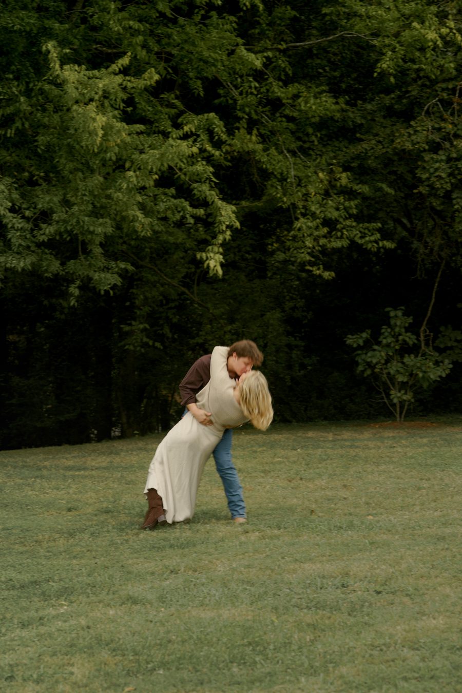 A dip and a kiss in an open field at the edge of the woods