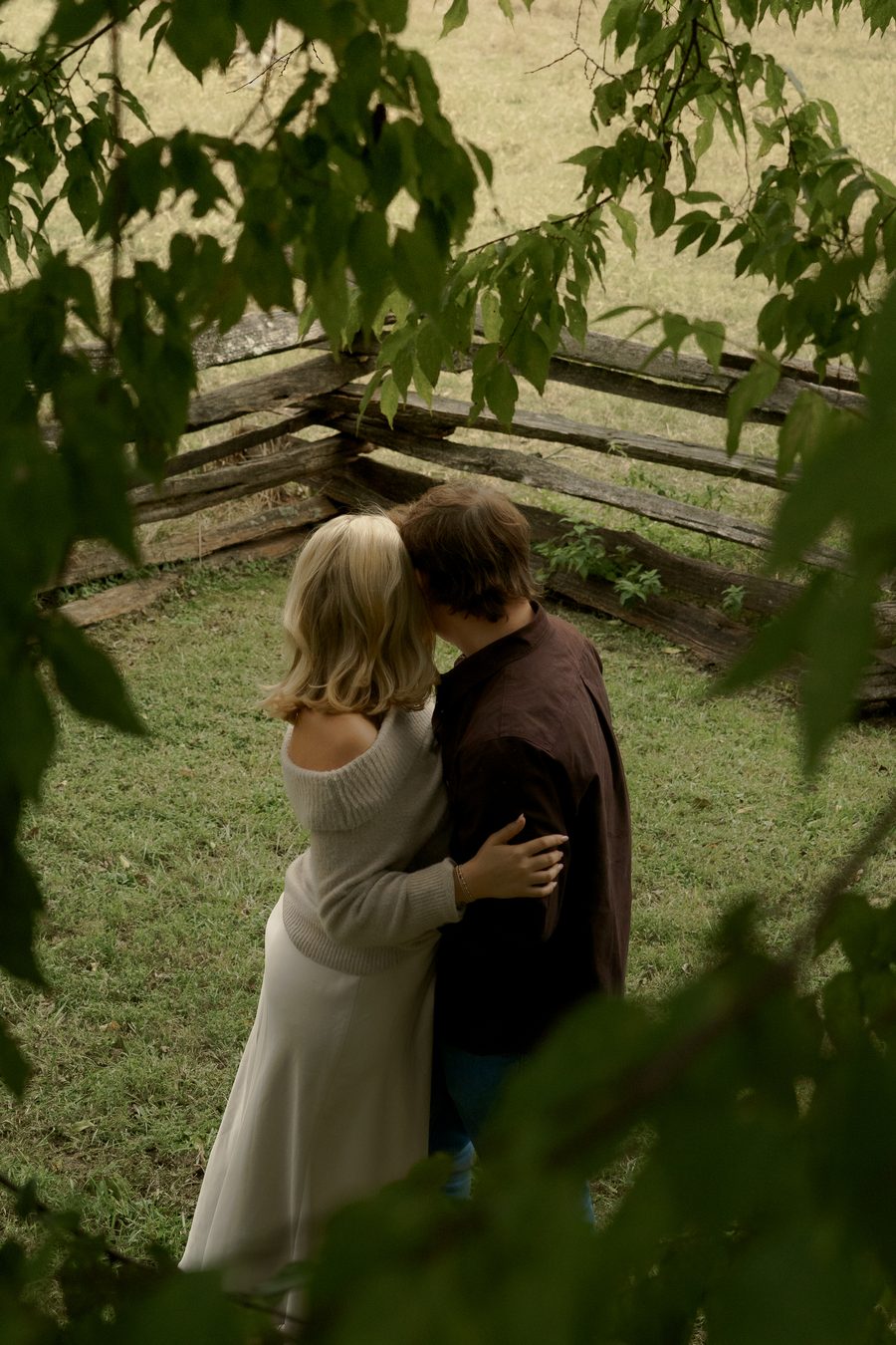 The couple framed through leaves at a rail fence