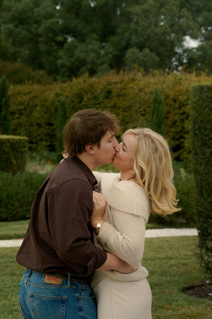 A kiss on a garden path between tall hedges