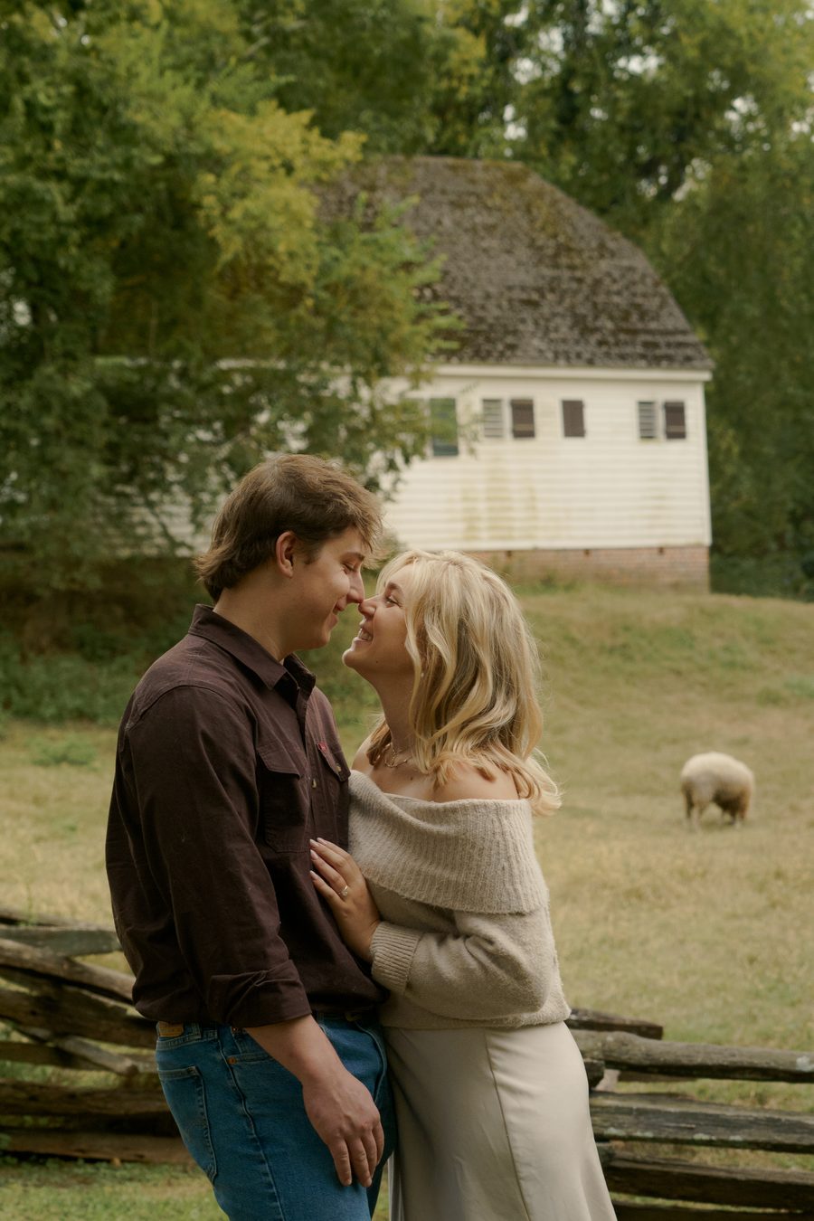 A near kiss by a fence, a white farm building behind them