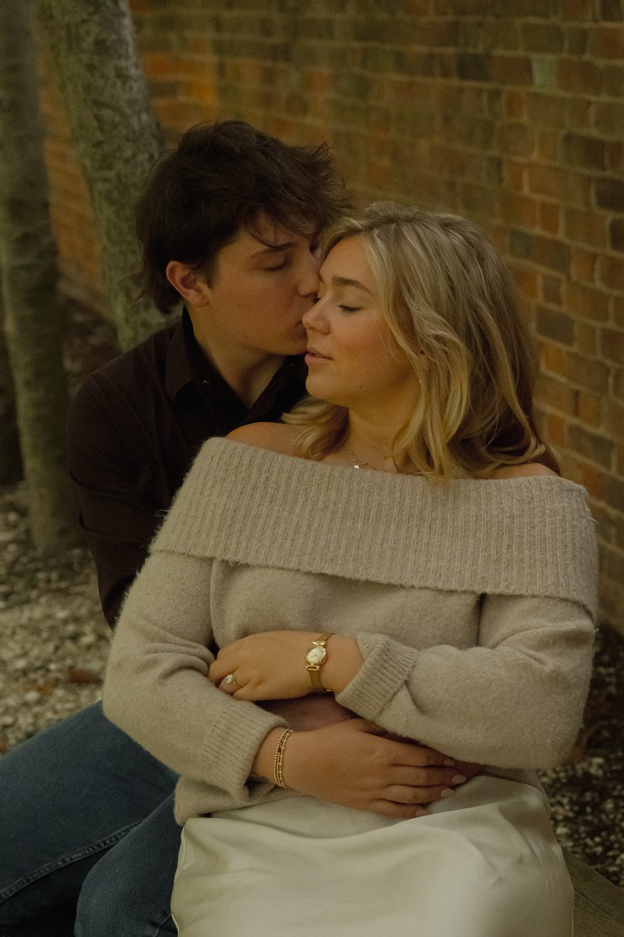 Seated against a brick wall, his face close to hers