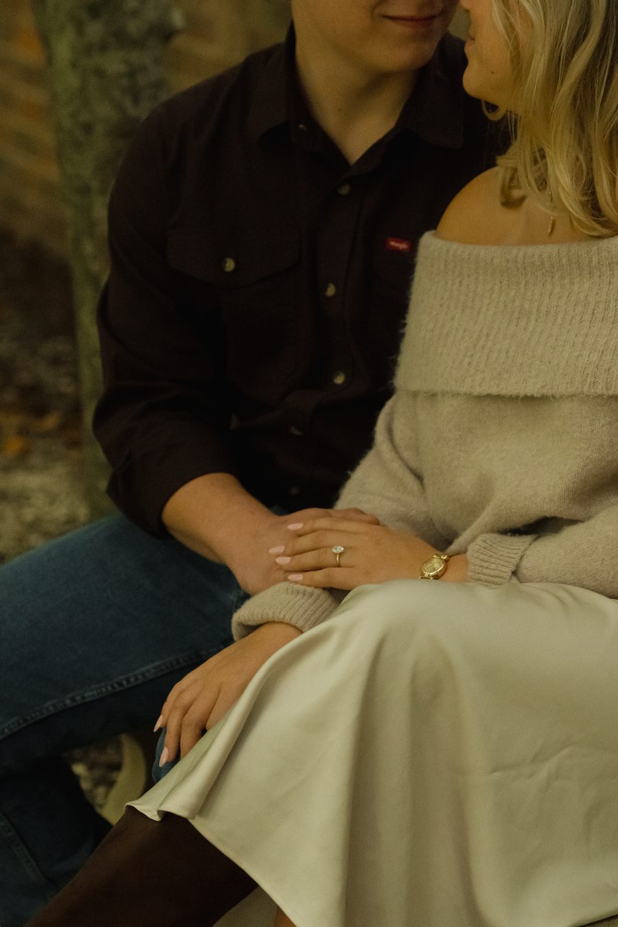 A close frame of the couple seated, her ring in view
