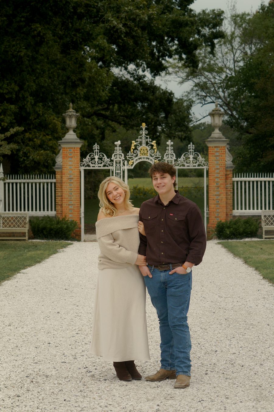 The couple on a gravel path before an iron garden gate