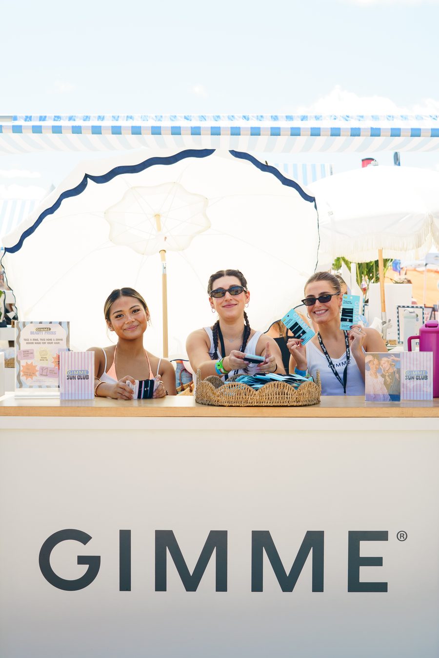 Three hosts behind a branded counter on the sand
