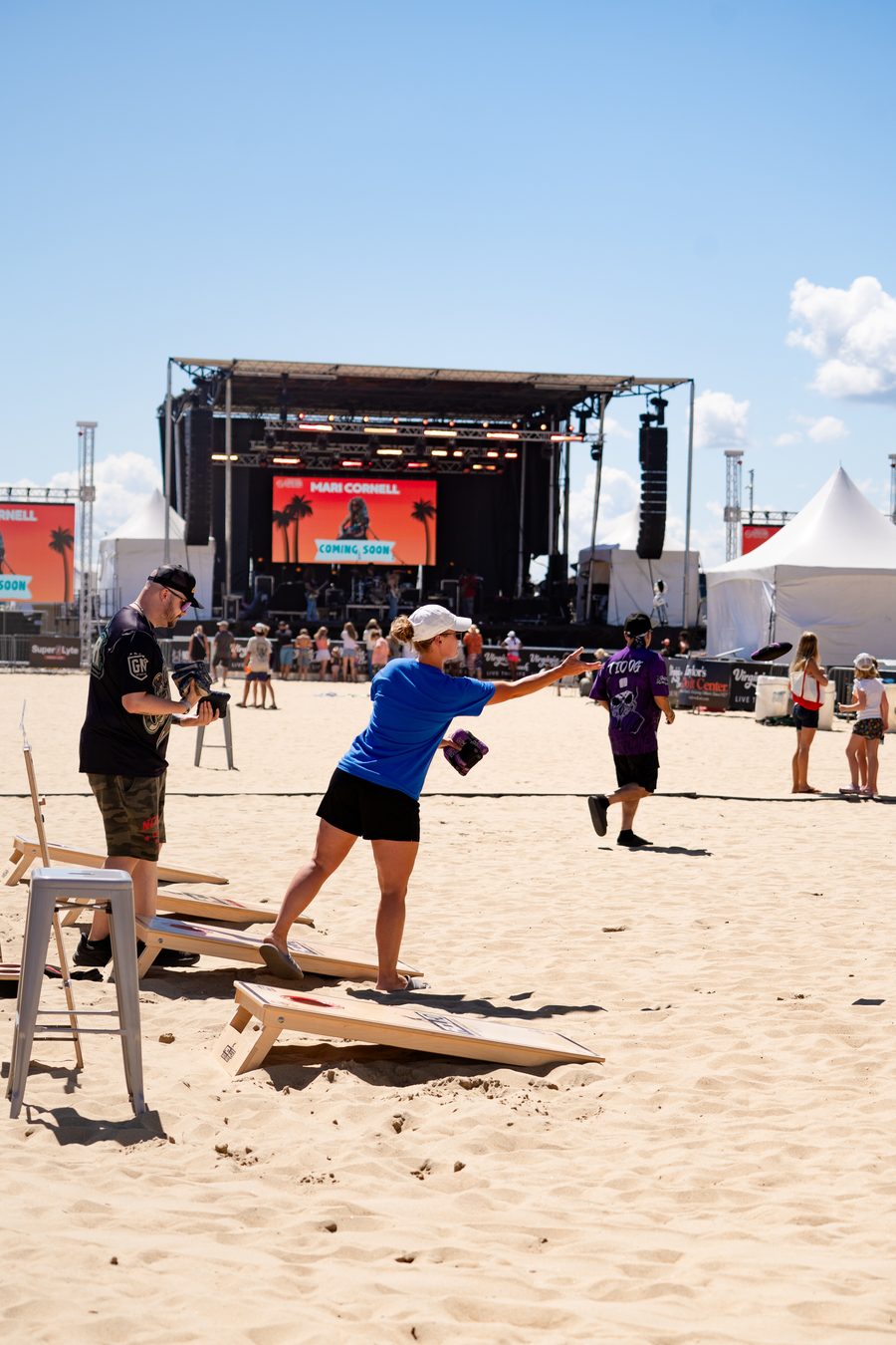 A cornhole game on the beach with the main stage behind