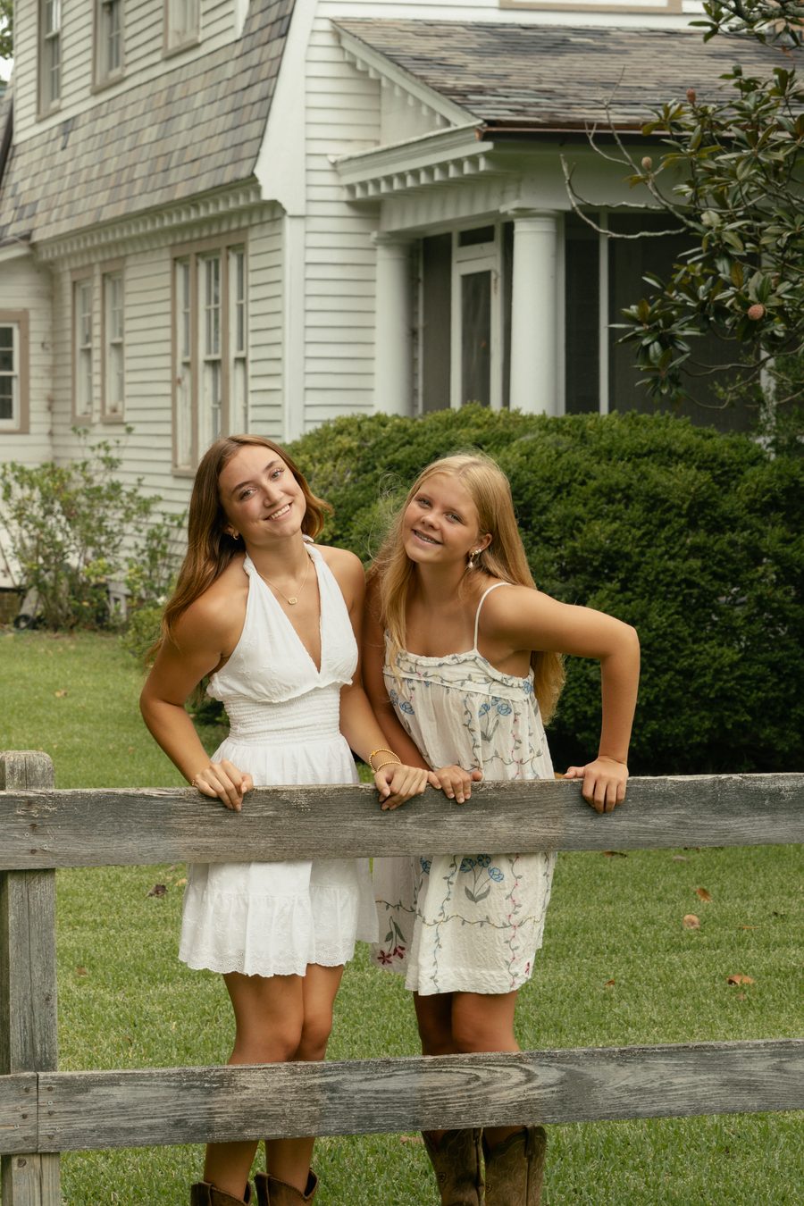 Two friends leaning on a split rail fence in white dresses