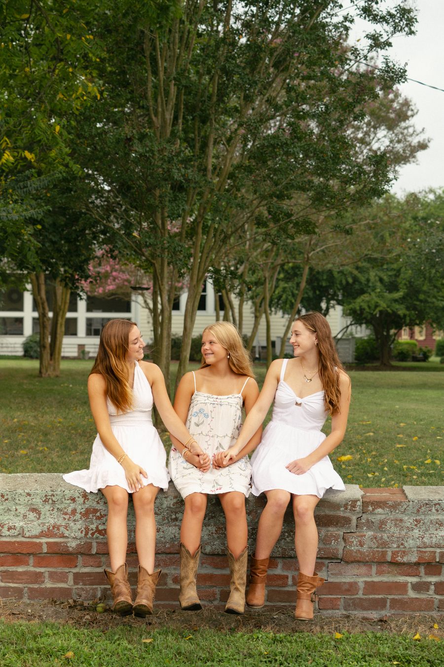 Three friends on a brick wall in matching white dresses