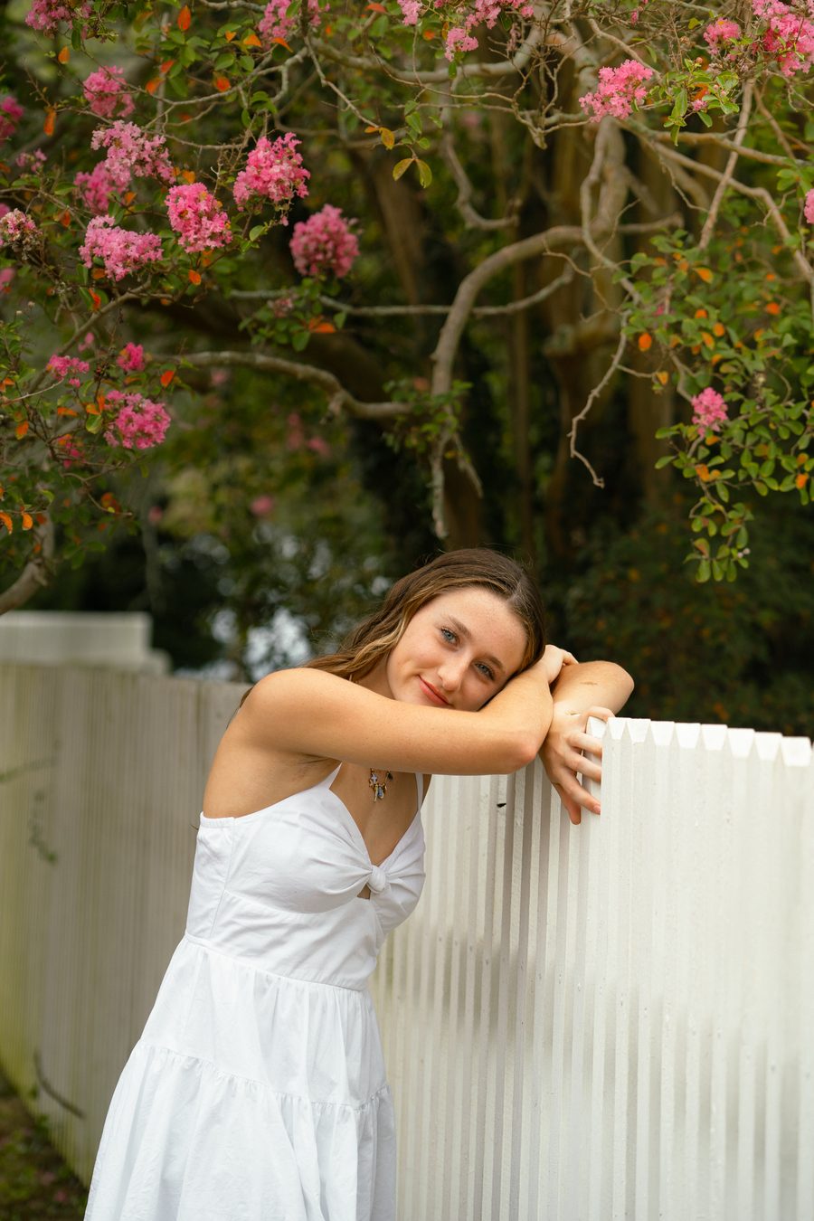 A portrait subject leaning on a picket fence beneath crape myrtle
