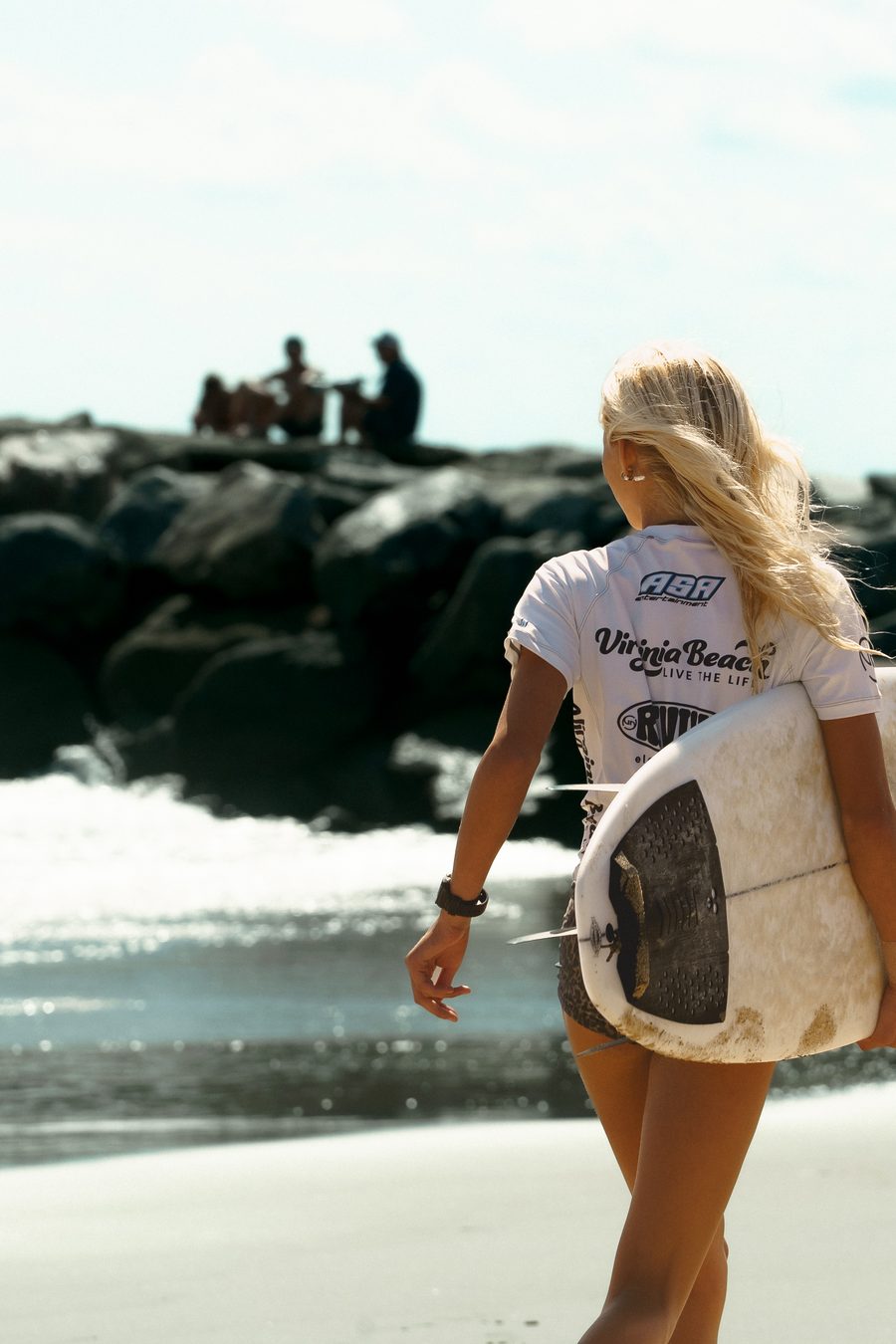 A surfer walking the shoreline with her board under one arm
